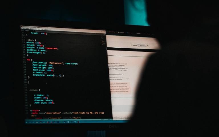 A shadowy figure using a computer with code on it