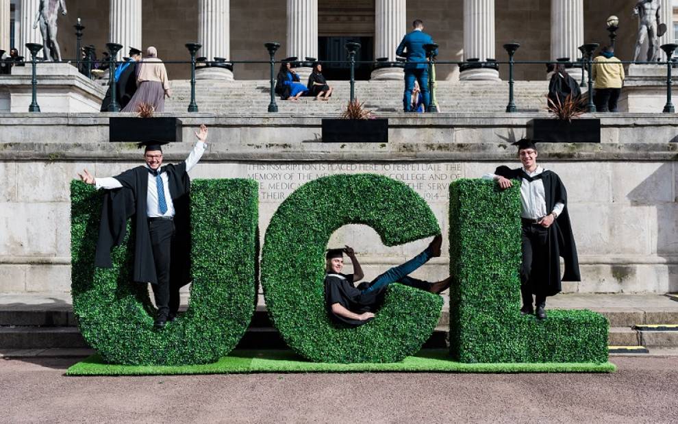 Student UCL Computer Science students at graduation 2022 in front of green UCL sign