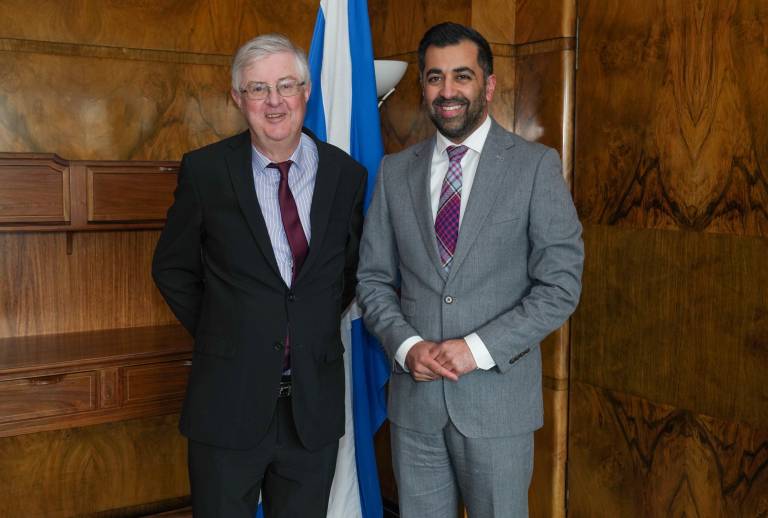 Welsh First Minister Mark Drakeford and Scottish First Minister Humza Yousaf are standing in a wood-panelled room posing for a picture. A Scottish flag is behind them.