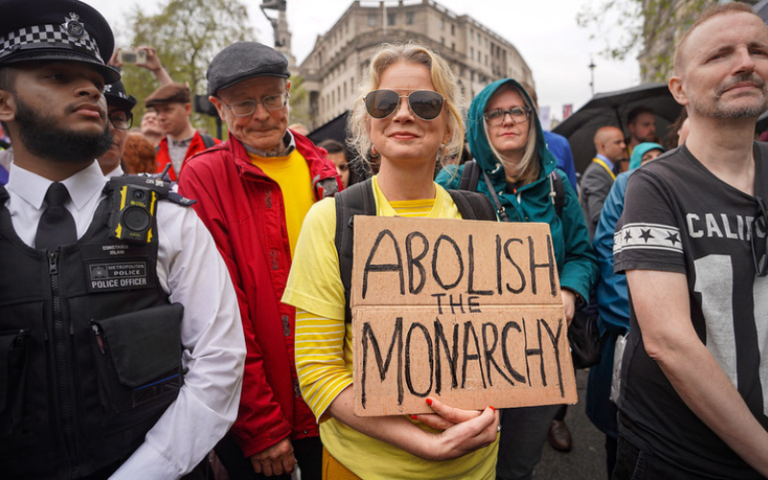 Protester holding cardboard placard reading 'Abolish the Monarchy'