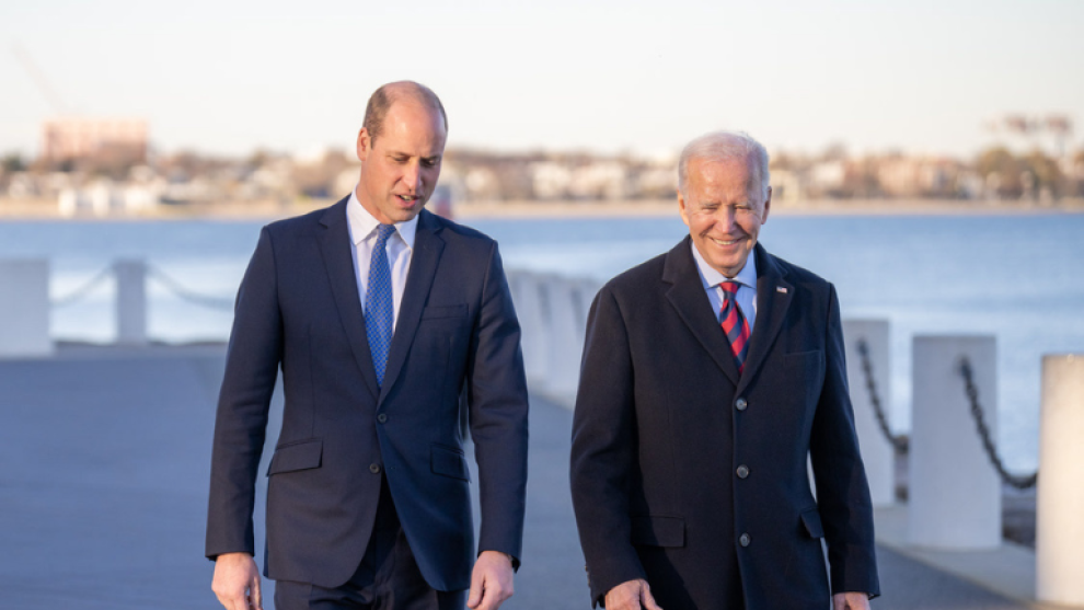 The Prince of Wales and Joe Biden walking past a body of water.