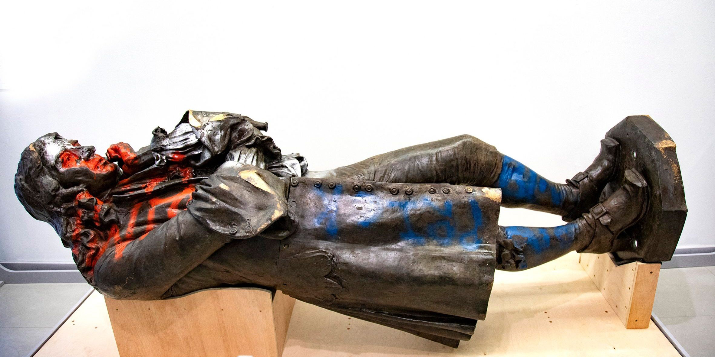 A statue of a man lying down on a museum plinth covered in paint