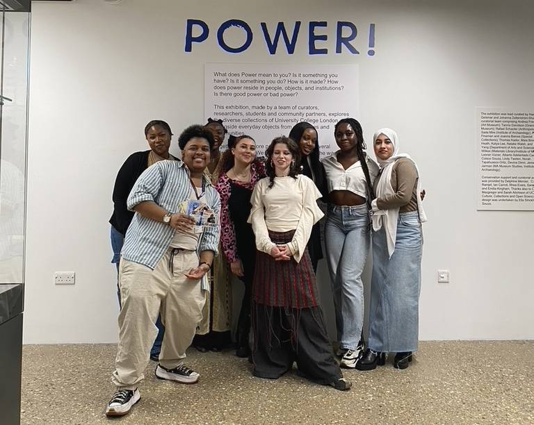 The Curating Power curators smiling and posing in front of the Power sign in the UCL Culture Lab