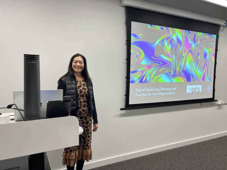 Ginny Wan smiling and standing next to a brightly-coloured screen reading 'Digital Marketing Planning and Practice for arts organisations'