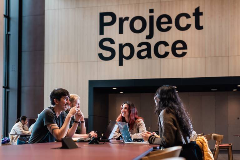 three people sitting around a table in the Marshgate building with the sign 'Project Space' behind them