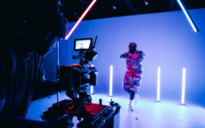 A person in an abstract costume is filmed on set under purple light