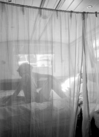Silhouette of woman sitting on bed behind curtain on canal boat