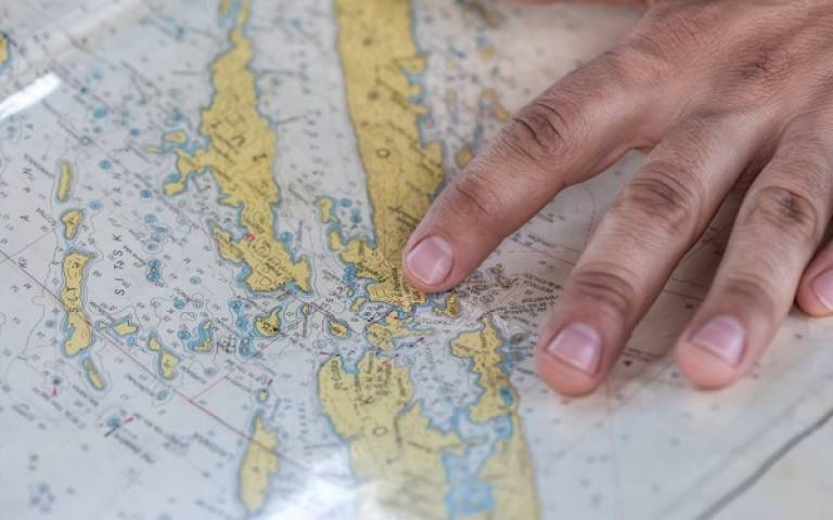 the photograph shows a hand placed across a map. the map is of a group of island surrounded by the ocean.. 