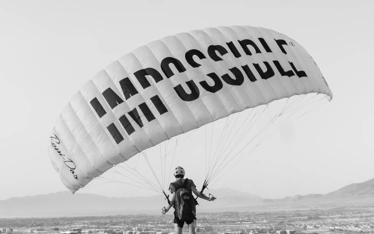 person in the air via parachute he parachute has the word impossible on it crossed out