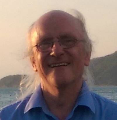 Photograph of Nick Tyler. His hair is grey and he wears glasses and a blue shirt while smiling at the camera.