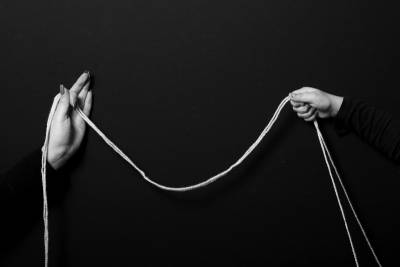 wo white hands holding a drooping string across a black background