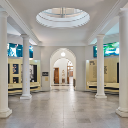 A gallery space with white walls and ceiling, white supporting columns and cases wrapped in gold vinyl