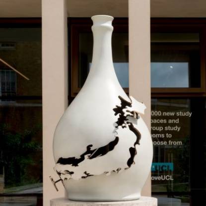 Large white bottle-shaped sculpture sitting on a plinth in front of a building