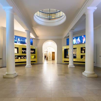 Photograph of a gallery space with pale polished floor, two display cases covered in gold vinyl, and four white painted columns