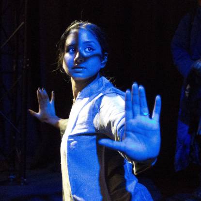 Female performer with arms outstretched under a blue light