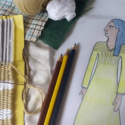 Close-up of a threaded homemade cardboard loom, two balls of yarn, some coloured pencils and a drawing of a simplified ancient Egyptian figure