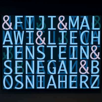 Colour photo showing a dark screen with bright blue neon letters spelling the names of different countries