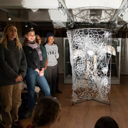 A group of young people stand beside a large white netting sculpture, positioned in a museum gallery
