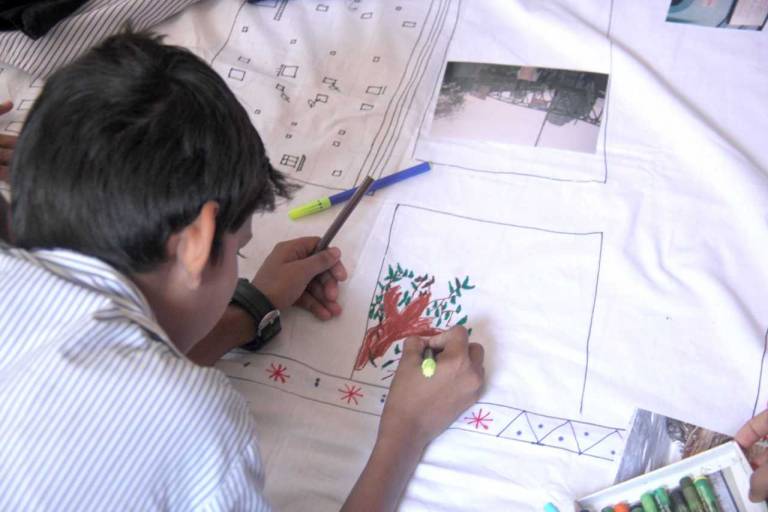 View over child's shoulder as he uses coloured pens to draw onto white fabric