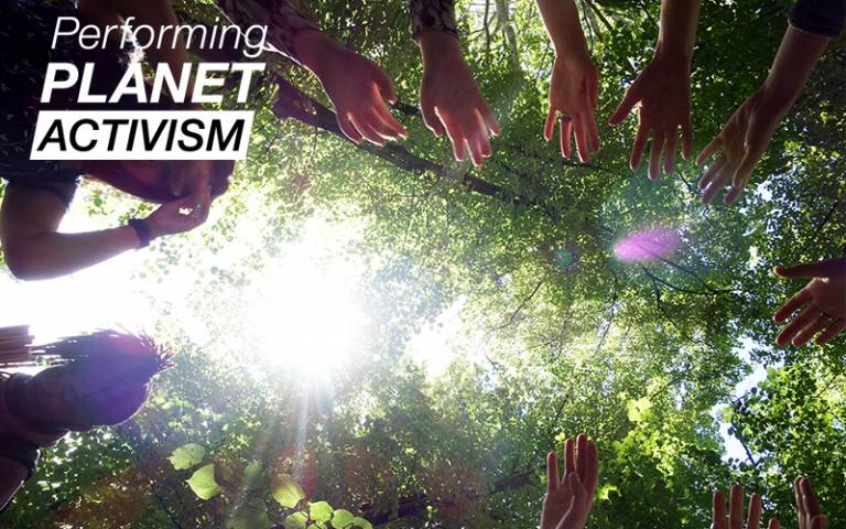 A view taken from below of a ring of hands reaching forward in a circle, with the tree canopy and the sun visible above them. The 'Performing Planet Activism' logo is in the top left corner.
