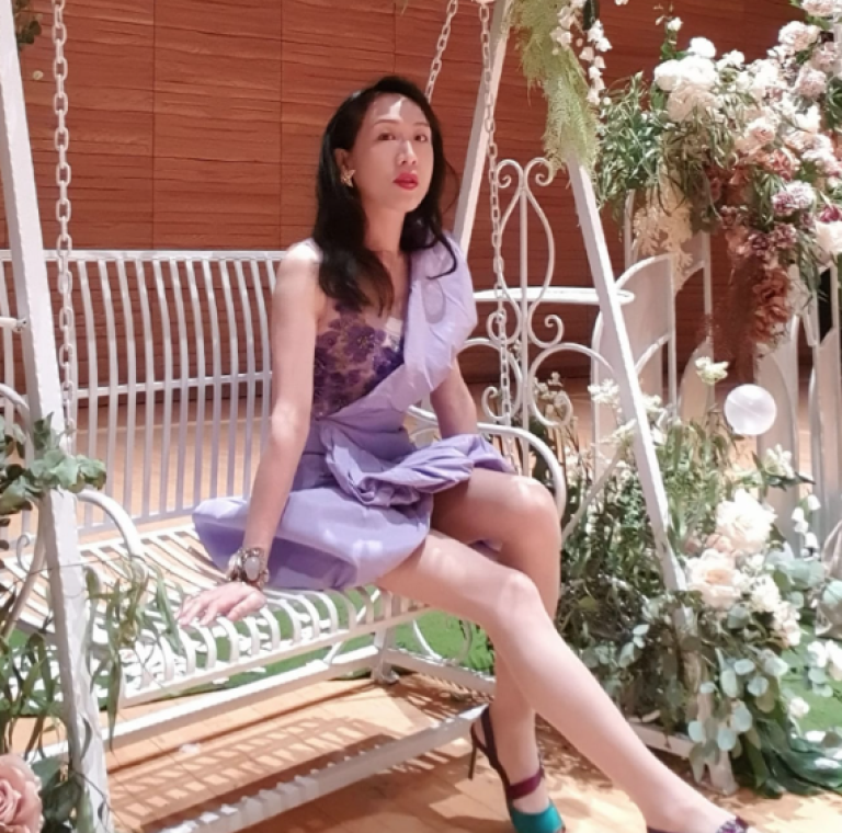 Picture of comedian Sony Chan sitting poised on a two person swing, wearing a lilac dress