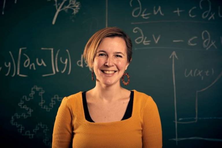 Dr Angelika Manhart smiles at the camera in front of a blackboard of mathematical equations