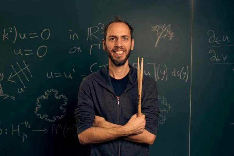 Bernhard Schimpelsberger holds a pair of drum sticks and stands in front of a blackboard
