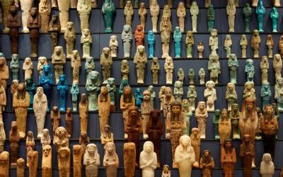 Photograph of a museum cabinet displaying rows of shabti figurines of different colours and sizes.
