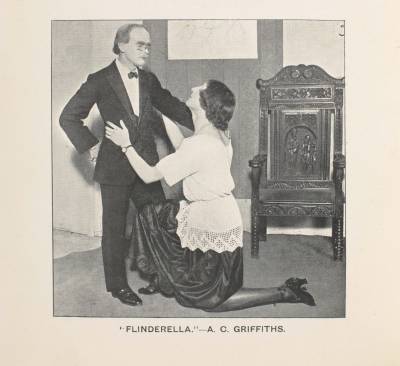 Archive photograph of two students performing in a play, one standing formally and wearing a dinner jacket, and the other in a white top and long dark skirt on one knee in front of him