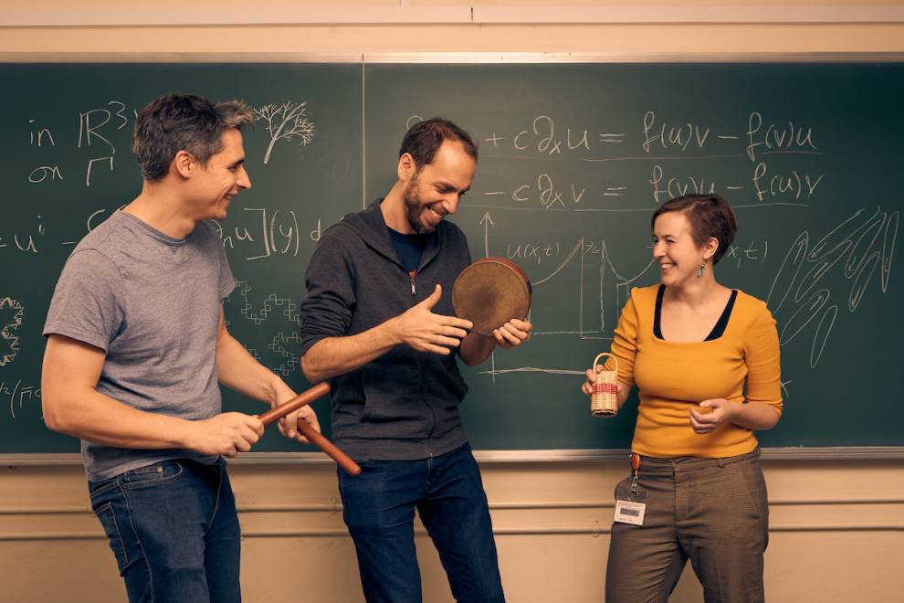 Dr David Hewett, Bernhard Schimpelsberger and Dr Angelika Manhart laugh together while playing instruments in front of a blackboard