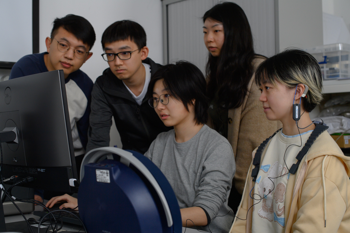 A group of 5 students gathered around a computer