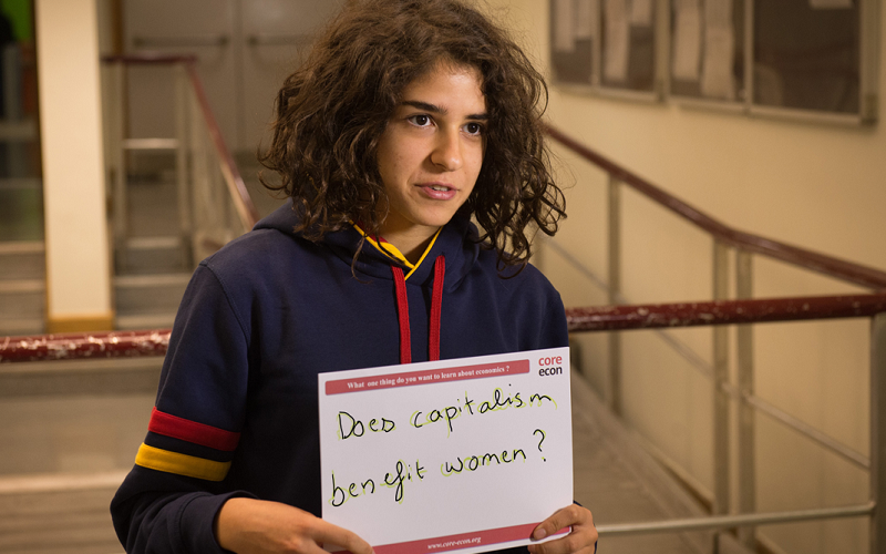 woman holding up sign saying does capitalism benefit women