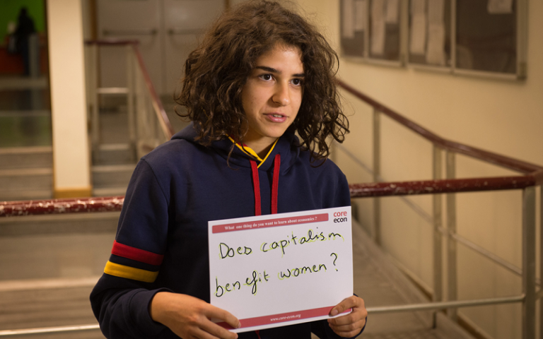 student holding a sign saying 'does capitalism benefit women?'