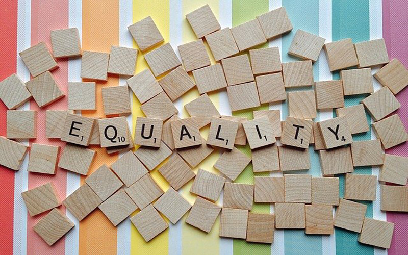 Smal wooded tiles spelling out the word equality on a rainbow background