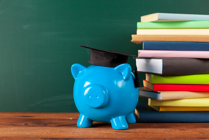 Image of a blue piggy bank wearing a graduation hat next to a stack of books