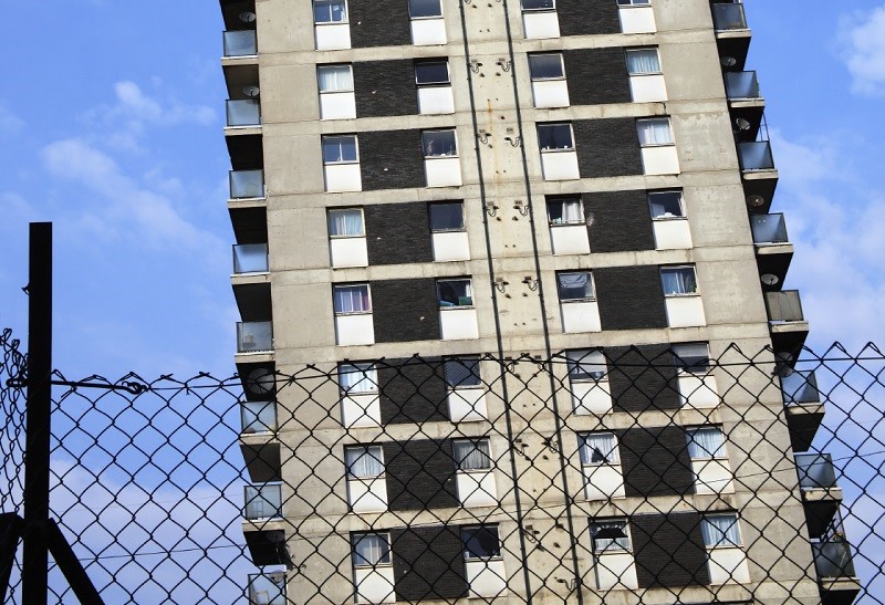 An image of a section of a tower block behind a chain link fence
