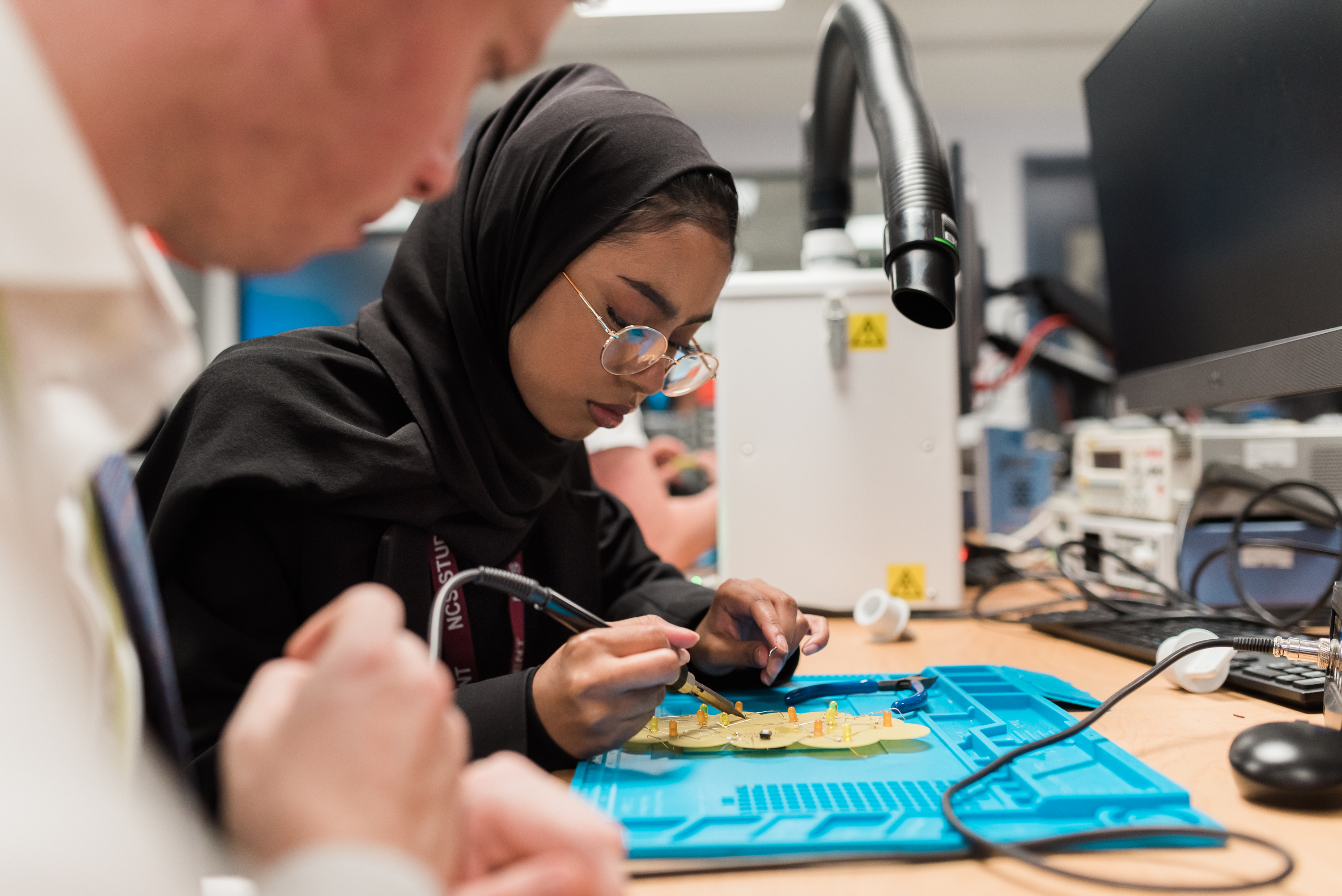 A young woman or girl wearing a hijab, using an engineering tool carefully over a task.