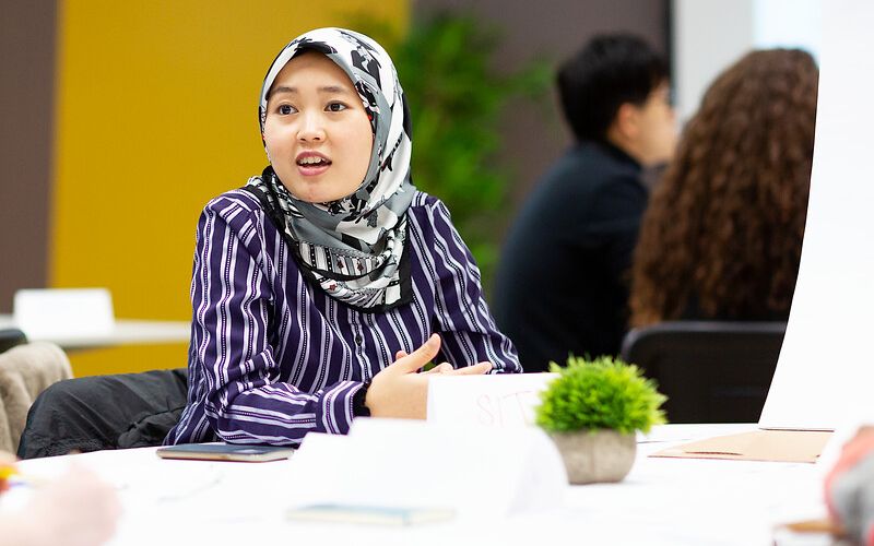 A woman in a hijab talking at a table.