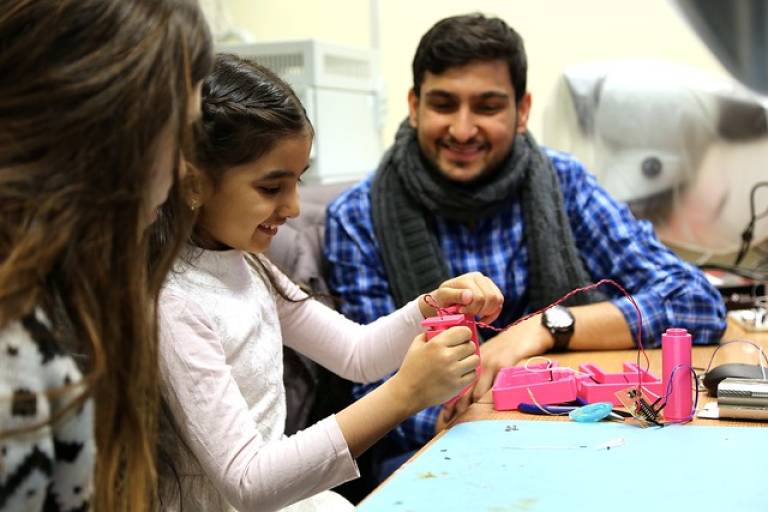 Two adults supervise a young girl practising an engineering activity.