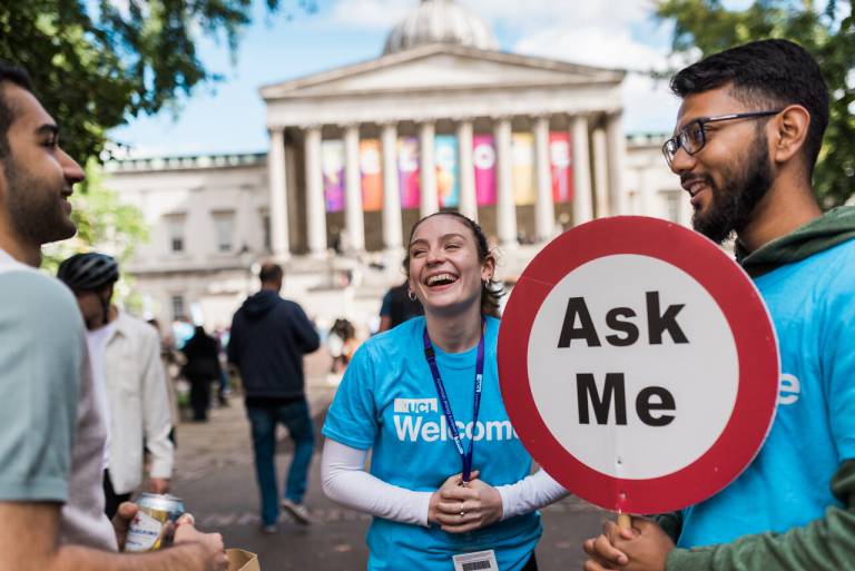 Students in front of the UCL Portico, one is holding a sign saying "ask me"