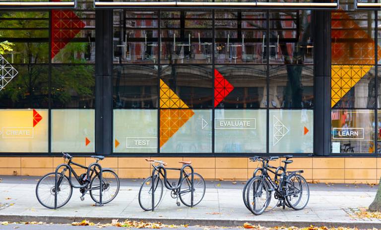 The front of the engineering building. The is a large window covering the whole wall, with triangle shapes of different colours on there (red yellow and orange). A few bicycles are parked in front of the building.
