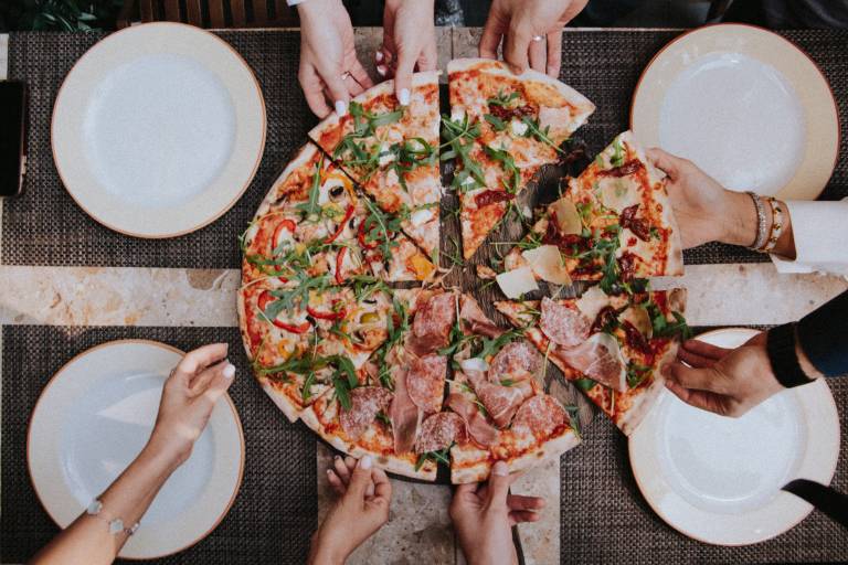 A group of people share a large pizza. You are only able to see the arms of the group.
