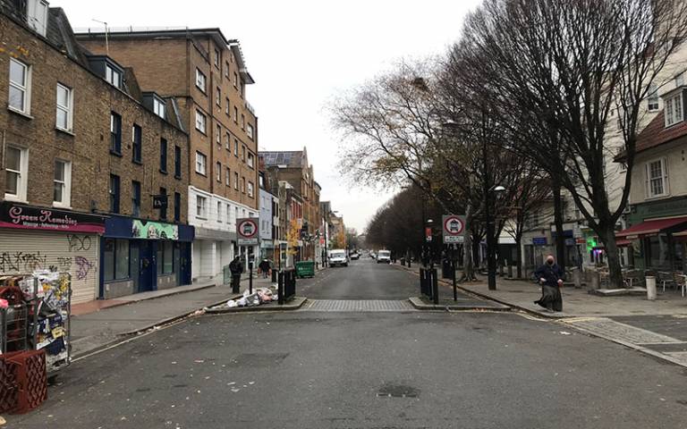 A street in Camden showing closed shop fronts, rubbish waiting to be collected, and people walking in the distance.