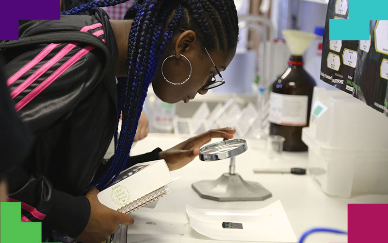 A student in a laboratory examines an item under a large magnifying glass