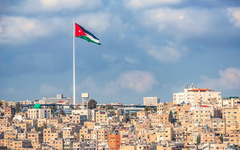  the flag of Jordan on the background of sky waves in the wind above the city of Amman