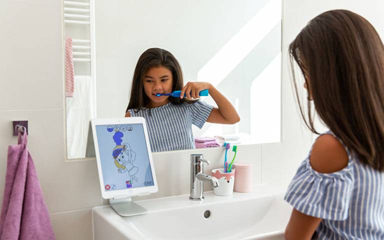 A child brushing their teeth in a bathroom looking at the Playbrush app on a tablet computer