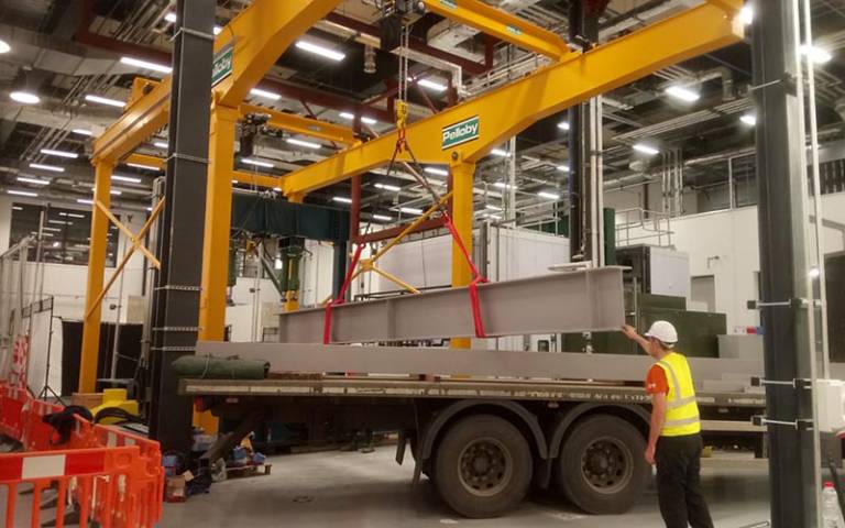Crane lowering a heavy load onto a flatbed lorry within a large building