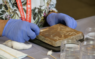 A conservation volunteer cleaning a tile with a cotton swab