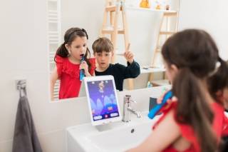 Two children looking at an ipad while brushing their teeth
