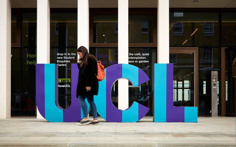 Student walking past a UCL building with giant letters spelling out UCL